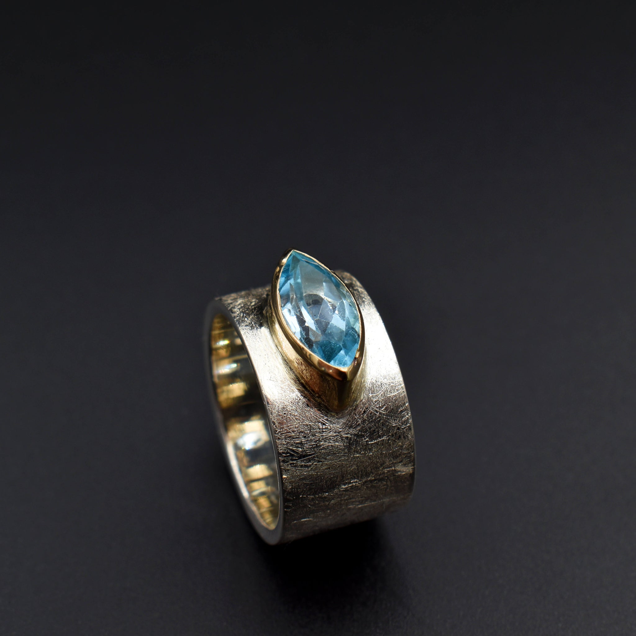 This document provides a crafted description for a handmade ring named 'Azure Elegance.' The ring features a subtly wide silver band with a matte finish and showcases a marquise-cut aquamarine at the top, embraced by a 14-karat yellow gold bezel. The description highlights the handcrafted nature, unique design, and key materials used, emphasizing its timeless beauty and modern allure. Additionally, the document includes suggested names and tags for the ring to enhance its discoverability on an eshop page.