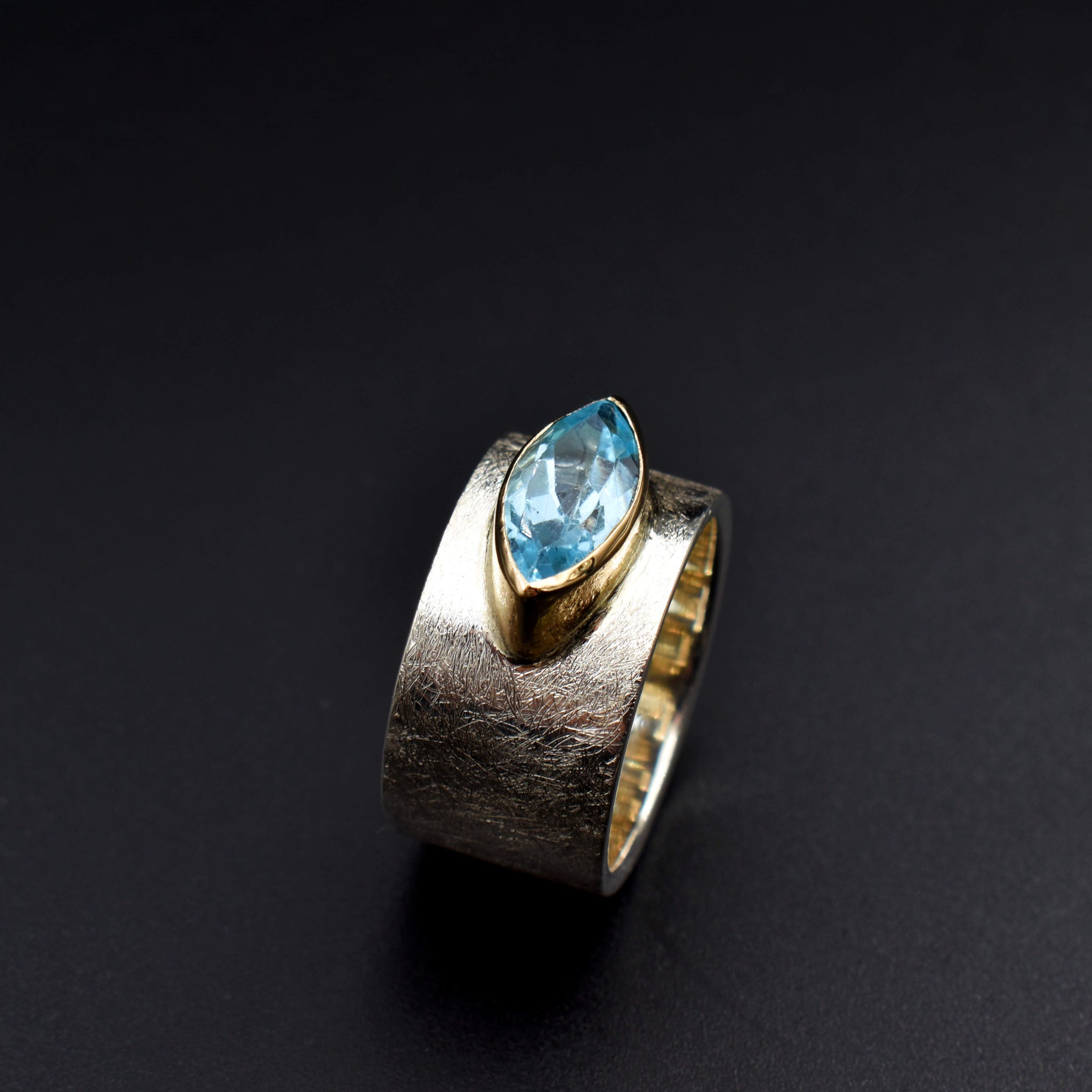 This document provides a crafted description for a handmade ring named 'Azure Elegance.' The ring features a subtly wide silver band with a matte finish and showcases a marquise-cut aquamarine at the top, embraced by a 14-karat yellow gold bezel. The description highlights the handcrafted nature, unique design, and key materials used, emphasizing its timeless beauty and modern allure. Additionally, the document includes suggested names and tags for the ring to enhance its discoverability on an eshop page.